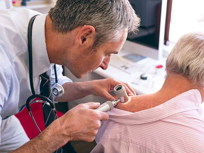 A male doctor checks a patients skin with a light.